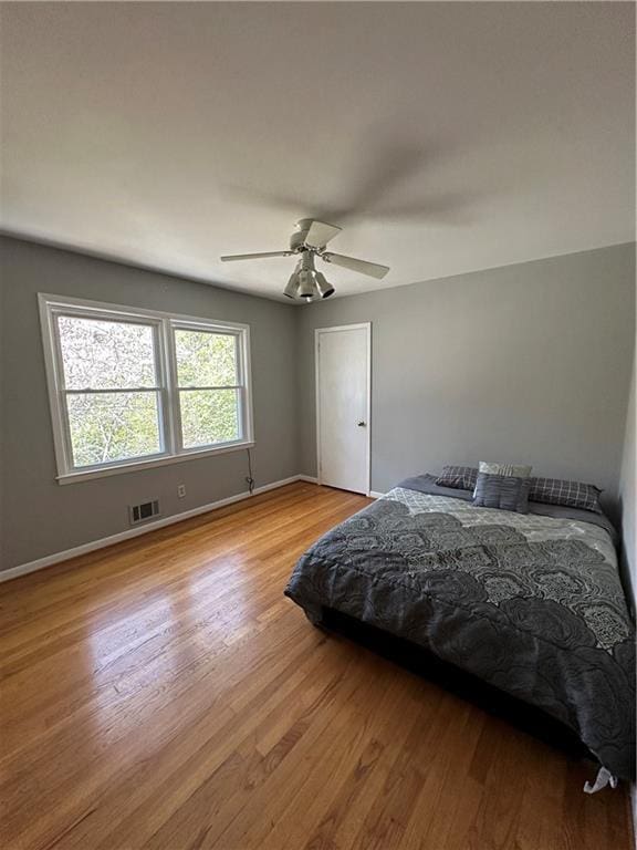 bedroom with ceiling fan, visible vents, baseboards, and wood finished floors