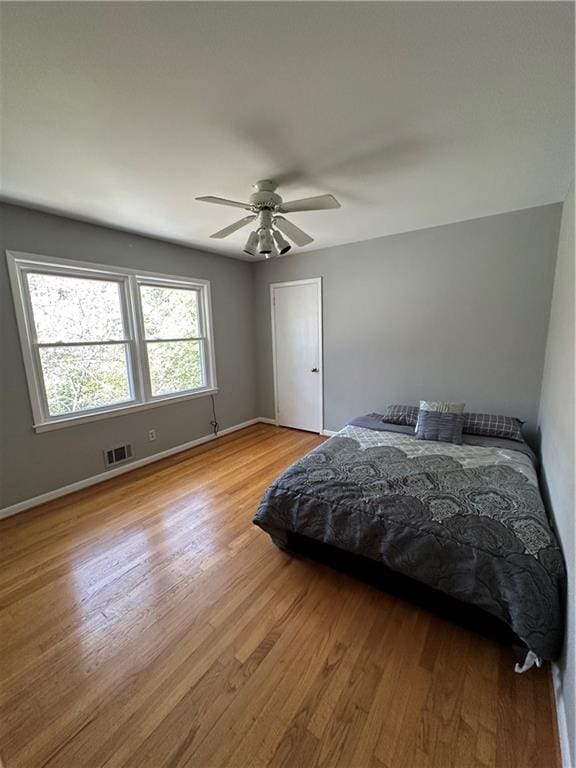 bedroom with a ceiling fan, light wood-style floors, visible vents, and baseboards