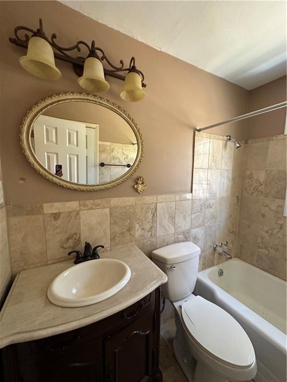 bathroom with vanity, wainscoting, shower / bathing tub combination, toilet, and tile walls