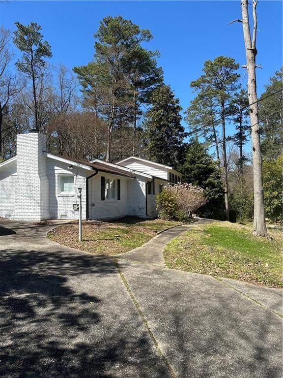 view of home's exterior featuring concrete driveway, brick siding, and a chimney