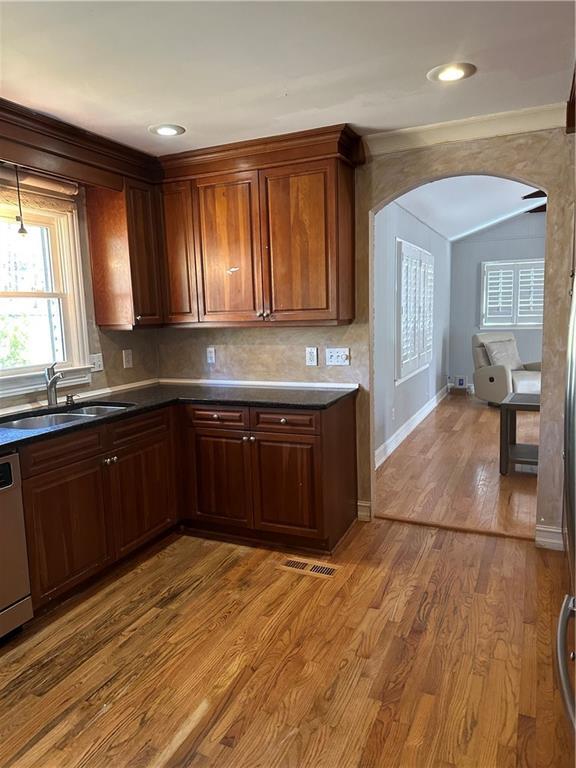 kitchen featuring a sink, dark countertops, wood finished floors, arched walkways, and dishwasher