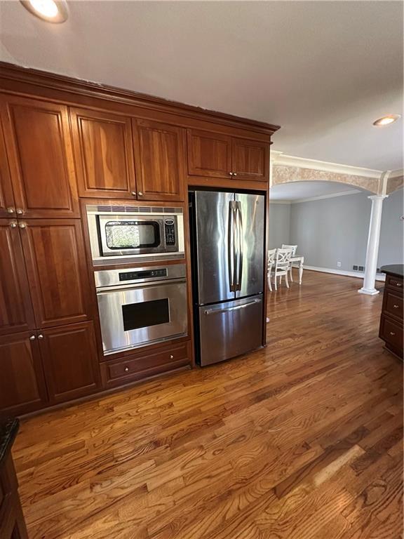 kitchen featuring appliances with stainless steel finishes, crown molding, ornate columns, and wood finished floors