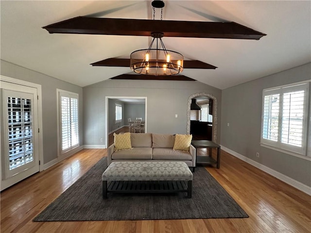 living area featuring a chandelier, vaulted ceiling with beams, baseboards, and wood finished floors