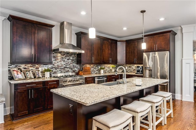 kitchen featuring high end appliances, wall chimney range hood, hanging light fixtures, and sink