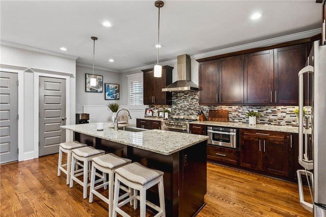 kitchen with a center island with sink, high quality appliances, pendant lighting, wall chimney exhaust hood, and sink