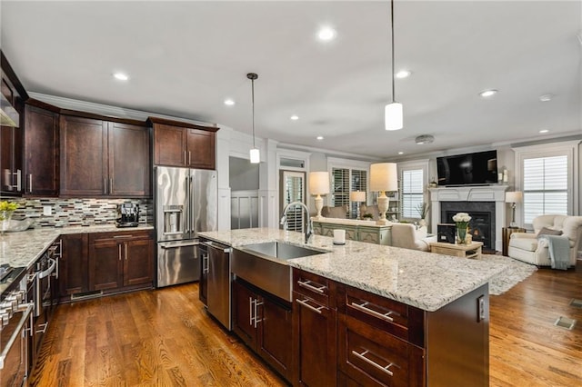 kitchen featuring wood-type flooring, appliances with stainless steel finishes, an island with sink, sink, and decorative light fixtures