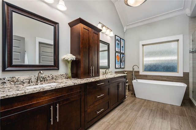 bathroom with lofted ceiling, tile walls, a bathing tub, vanity, and crown molding