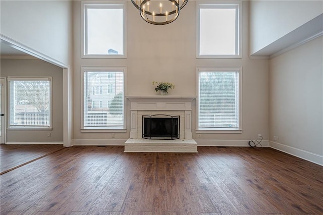 unfurnished living room with dark wood-type flooring, a chandelier, a brick fireplace, and a high ceiling