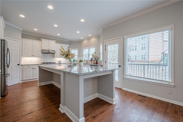 kitchen with white cabinetry, light stone counters, a center island with sink, stainless steel fridge, and a healthy amount of sunlight