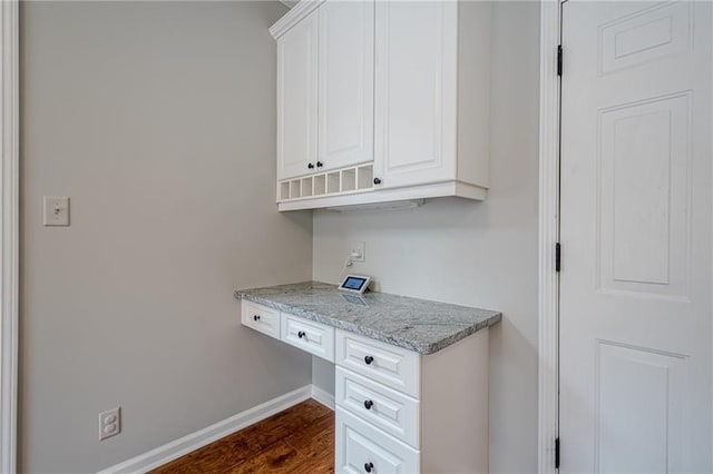 kitchen with light stone counters, built in desk, dark wood-type flooring, and white cabinets