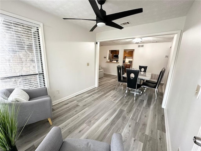 living room featuring ceiling fan, light hardwood / wood-style flooring, and a textured ceiling