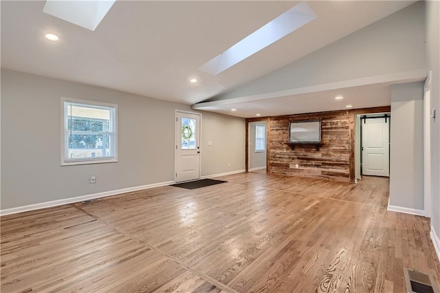 unfurnished living room with lofted ceiling with skylight, a barn door, and light hardwood / wood-style floors