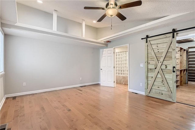 unfurnished bedroom featuring vaulted ceiling, a barn door, wood-type flooring, and ensuite bathroom