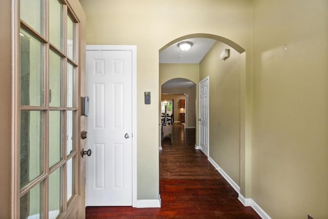 hall with wood finished floors, baseboards, and arched walkways