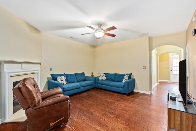 living room with arched walkways, a ceiling fan, wood finished floors, a fireplace, and baseboards