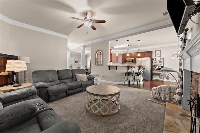 living room featuring crown molding, baseboards, ornate columns, a fireplace with raised hearth, and a ceiling fan