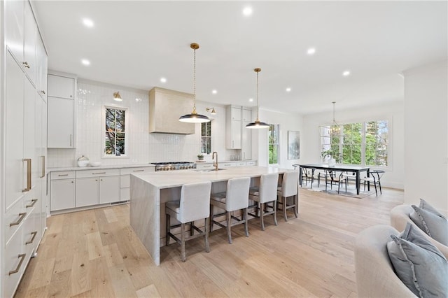 kitchen featuring a kitchen island with sink, pendant lighting, white cabinets, and light wood-type flooring