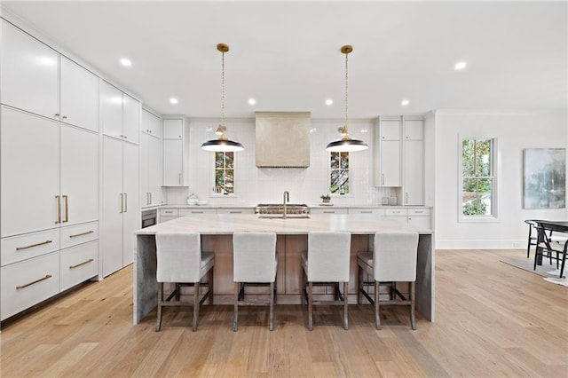 kitchen with a breakfast bar area, hanging light fixtures, tasteful backsplash, white cabinets, and a large island with sink