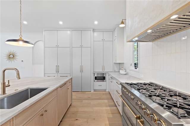 kitchen with light brown cabinetry, sink, decorative light fixtures, white cabinets, and wall chimney range hood