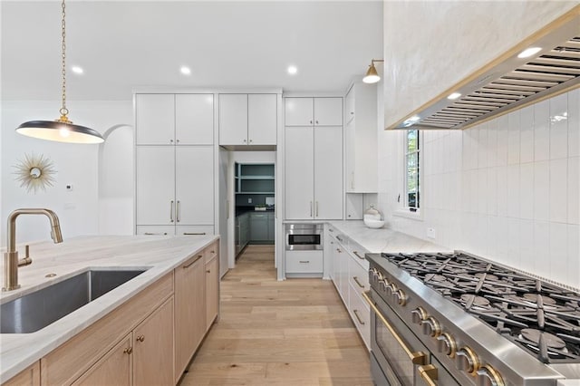 kitchen featuring light brown cabinetry, sink, light stone counters, white cabinets, and wall chimney range hood