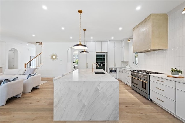 kitchen with premium range hood, pendant lighting, white cabinetry, range with two ovens, and a large island