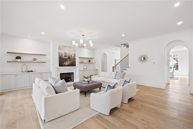 living room with a premium fireplace, crown molding, an inviting chandelier, and light wood-type flooring