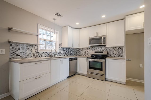 kitchen with sink, light tile patterned floors, hanging light fixtures, appliances with stainless steel finishes, and white cabinets