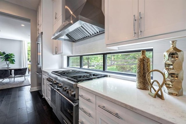 kitchen featuring wall chimney range hood, light stone counters, dark hardwood / wood-style flooring, range with two ovens, and white cabinets