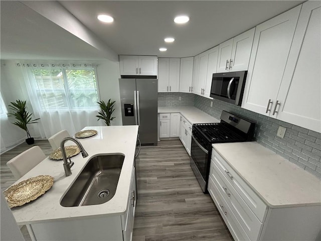 kitchen with sink, white cabinetry, light stone counters, appliances with stainless steel finishes, and a kitchen island with sink