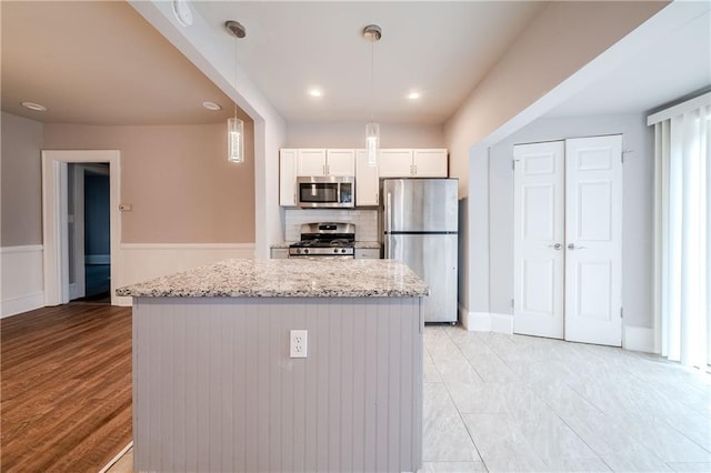 kitchen with appliances with stainless steel finishes, white cabinets, decorative backsplash, hanging light fixtures, and light stone counters