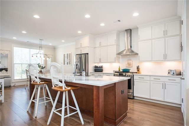 kitchen with a kitchen island with sink, visible vents, appliances with stainless steel finishes, wall chimney exhaust hood, and crown molding