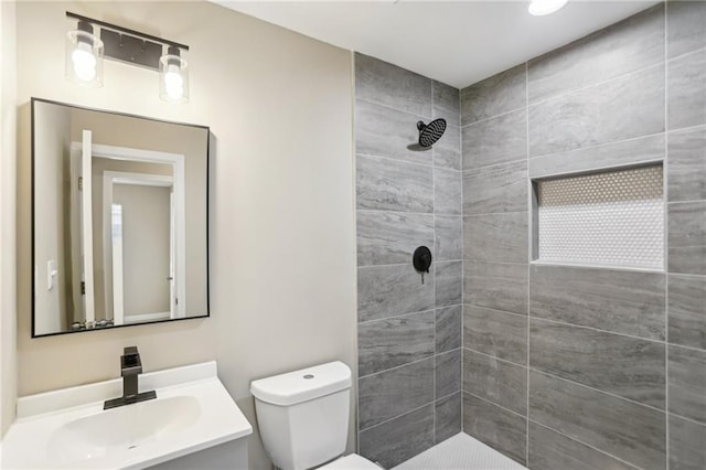 bathroom featuring vanity, a tile shower, and toilet