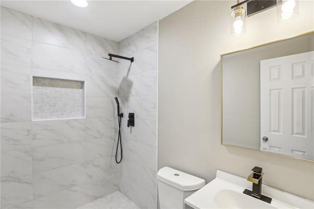 bathroom featuring a tile shower, vanity, and toilet