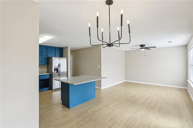 kitchen featuring stainless steel refrigerator with ice dispenser, blue cabinets, pendant lighting, light stone countertops, and light hardwood / wood-style floors