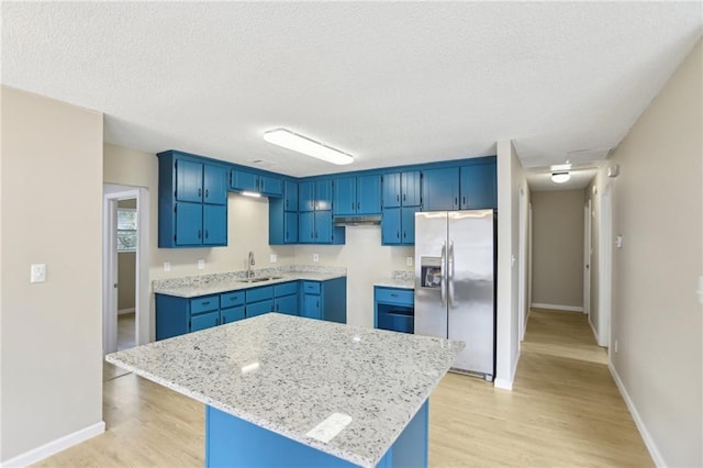 kitchen with blue cabinetry, sink, stainless steel fridge, a kitchen island, and light stone countertops