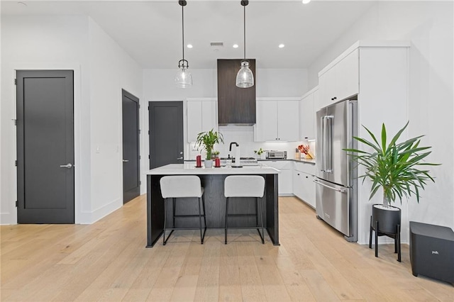 kitchen with white cabinetry, hanging light fixtures, light hardwood / wood-style floors, high quality fridge, and a center island with sink