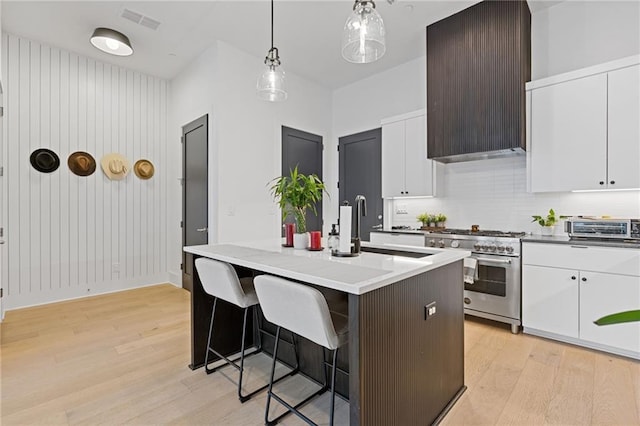 kitchen with white cabinets, pendant lighting, a kitchen island with sink, and stainless steel range