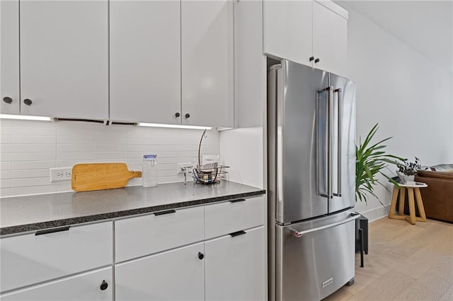 kitchen featuring tasteful backsplash, high quality fridge, dark stone countertops, white cabinets, and light hardwood / wood-style floors