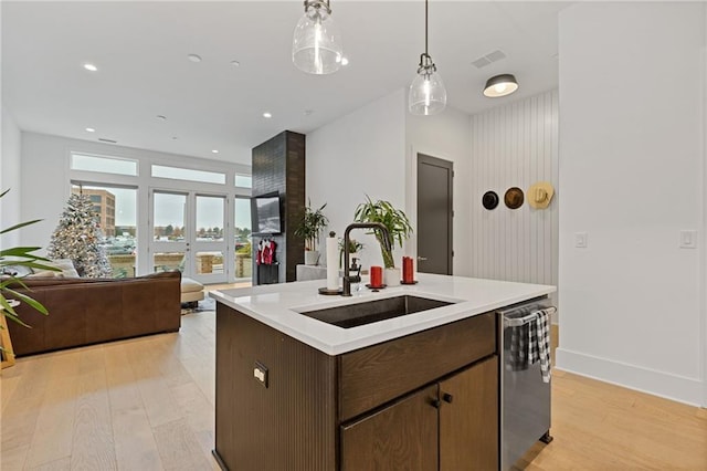 kitchen featuring dishwasher, a center island with sink, sink, light wood-type flooring, and decorative light fixtures