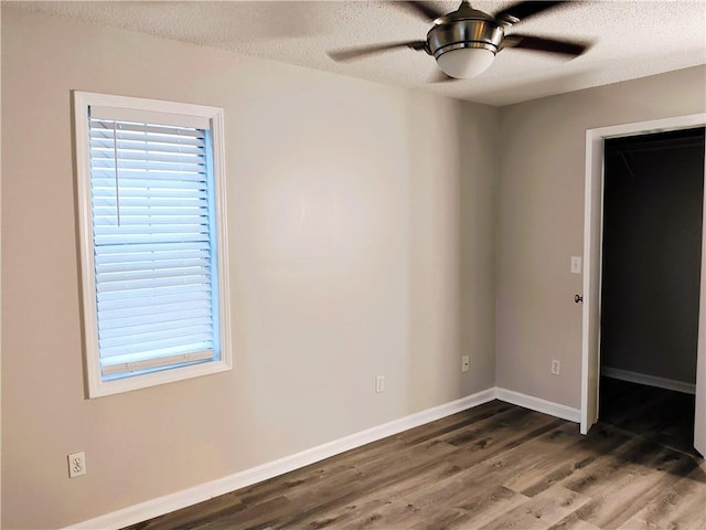 unfurnished bedroom with a spacious closet, a textured ceiling, dark hardwood / wood-style floors, and ceiling fan