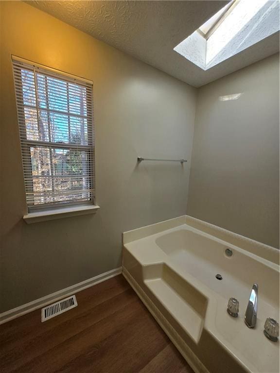 bathroom with hardwood / wood-style floors, a textured ceiling, a bath, and a skylight