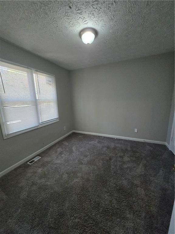 unfurnished room with a textured ceiling and dark colored carpet