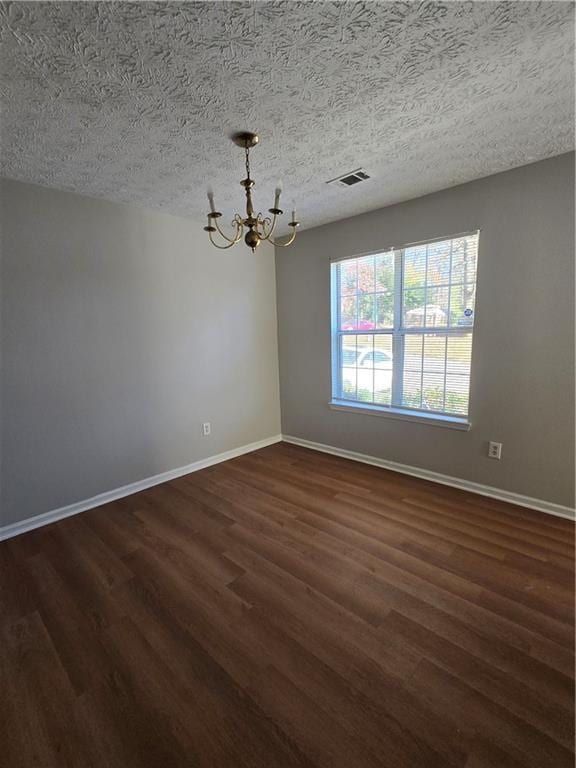 spare room with a textured ceiling, dark wood-type flooring, and a chandelier