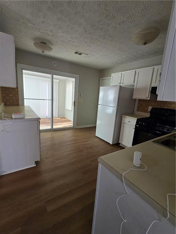 kitchen with dark hardwood / wood-style flooring, black gas range oven, sink, white cabinets, and white fridge