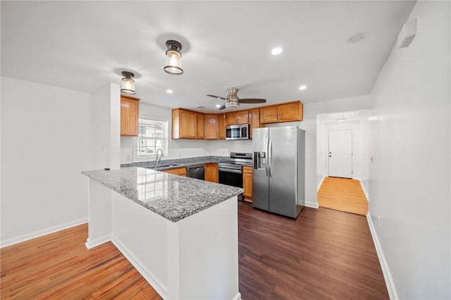 kitchen featuring dark wood-type flooring, sink, kitchen peninsula, stone counters, and stainless steel appliances