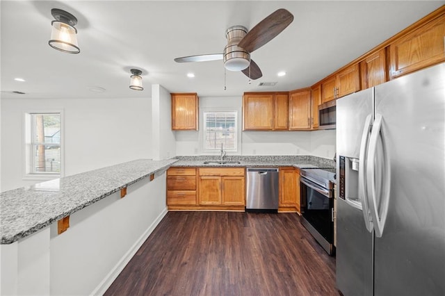 kitchen with sink, appliances with stainless steel finishes, dark hardwood / wood-style floors, light stone counters, and kitchen peninsula