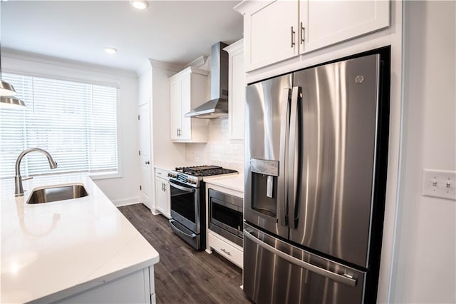 kitchen with appliances with stainless steel finishes, white cabinetry, sink, light stone counters, and wall chimney range hood