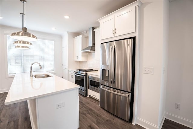 kitchen with appliances with stainless steel finishes, white cabinetry, hanging light fixtures, an island with sink, and wall chimney exhaust hood