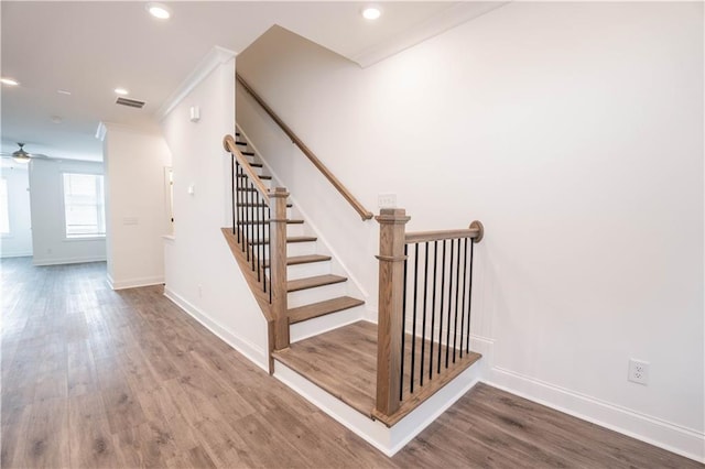 stairs with crown molding, wood-type flooring, and ceiling fan