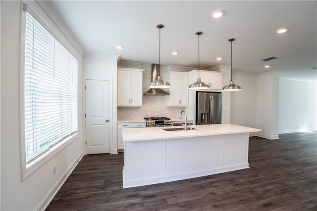 kitchen with wall chimney exhaust hood, sink, a center island with sink, pendant lighting, and stainless steel appliances